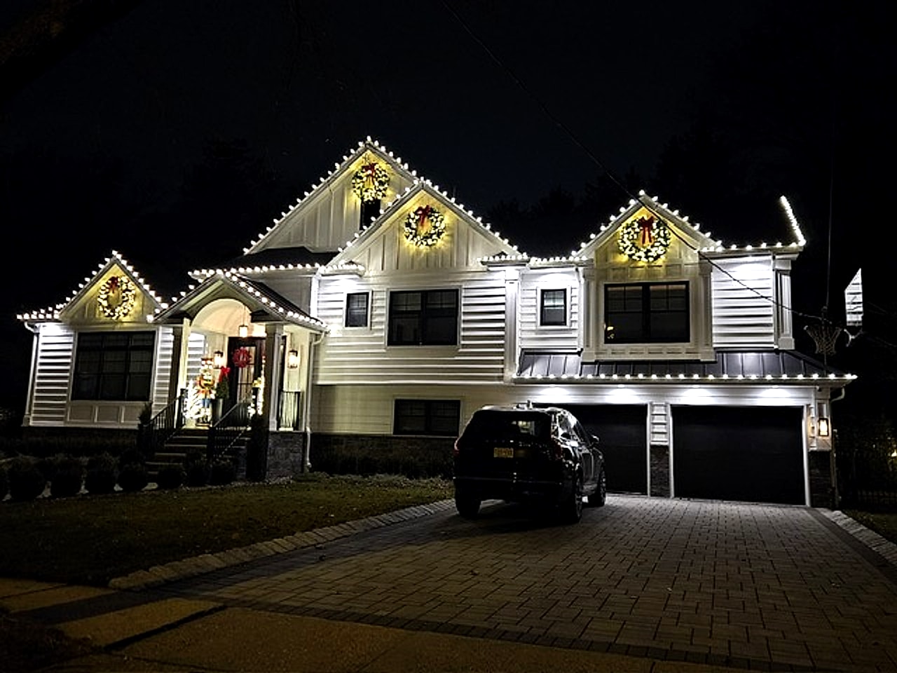 Warm white C9 LED roofline holiday lighting with wreaths on a luxury home in Bergen County, NJ