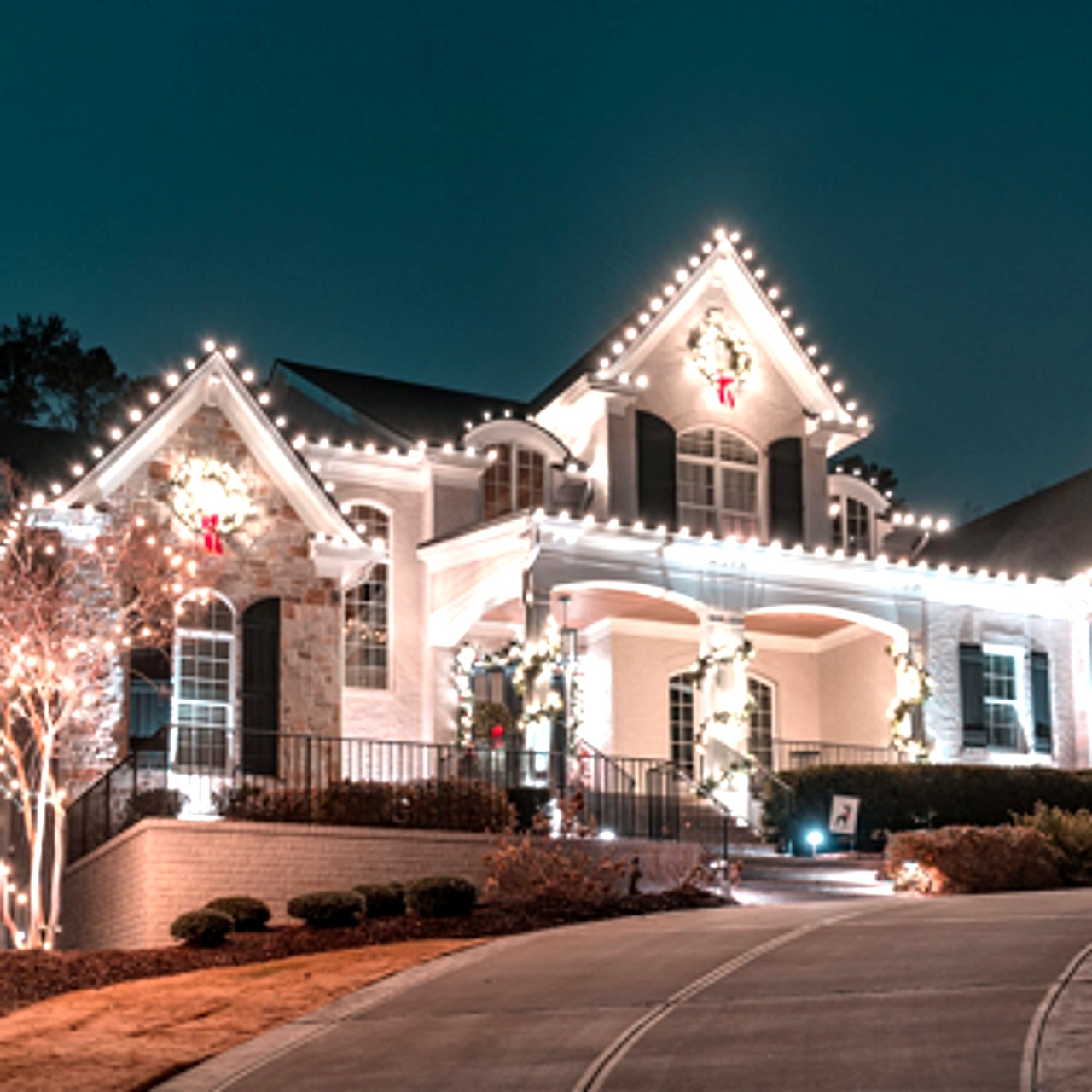 Warm white holiday lighting wrapped around entrance columns and roofline of a colonial home