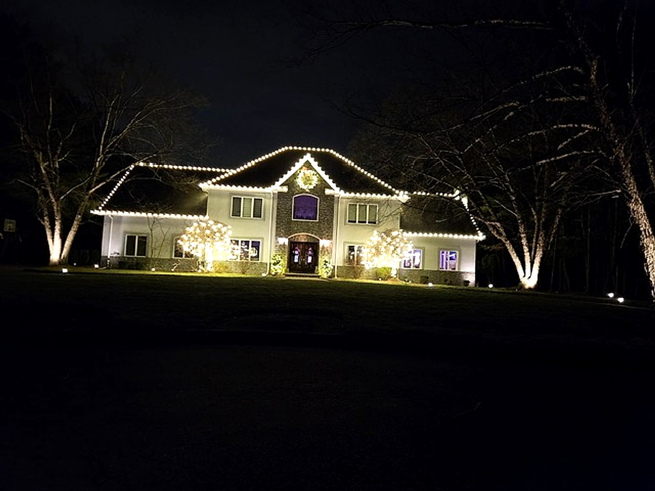 Warm white holiday lighting on entrance shrubs and illuminated trees at a luxury home