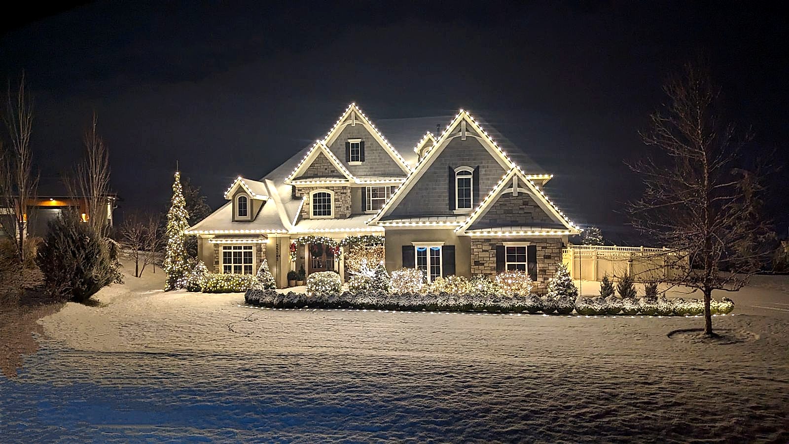Warm white C9 LED roofline and bush holiday lighting install on a stone estate home