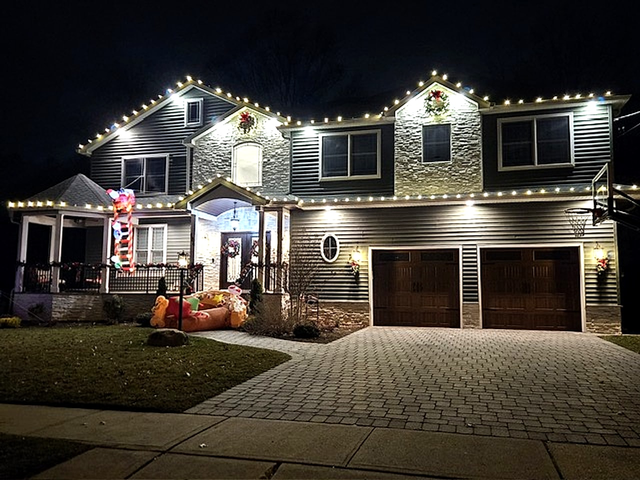 Warm white C9 LED roofline holiday lighting on a luxury home with paver driveway